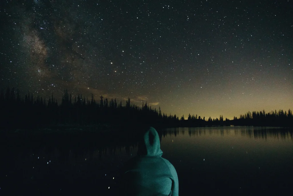 A traveller gazing across a calm lake under a star-filled night sky