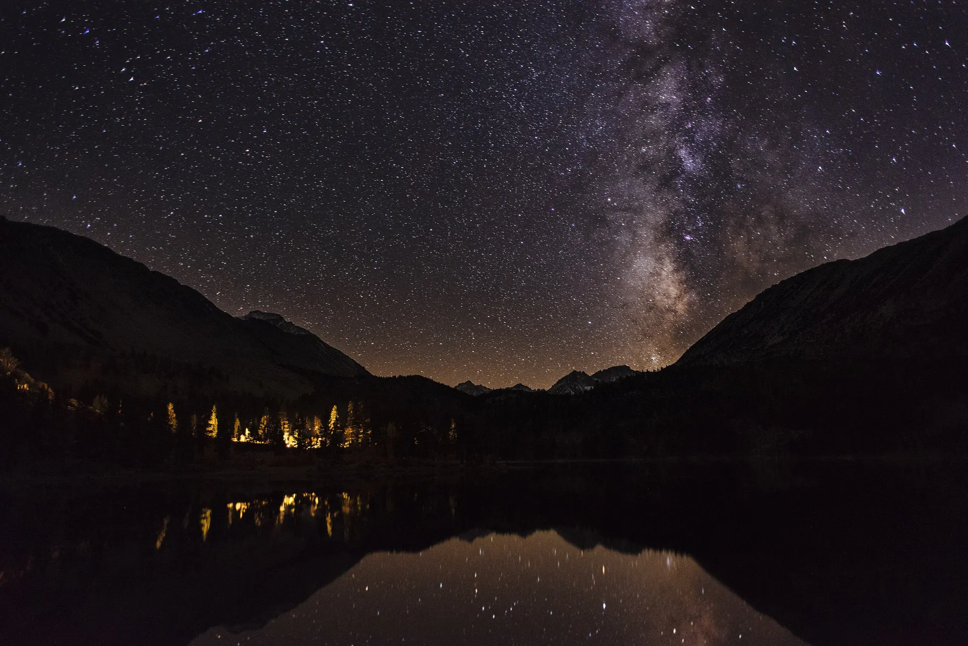 The Milky Way arching over dark mountains reflected in a still lake at night