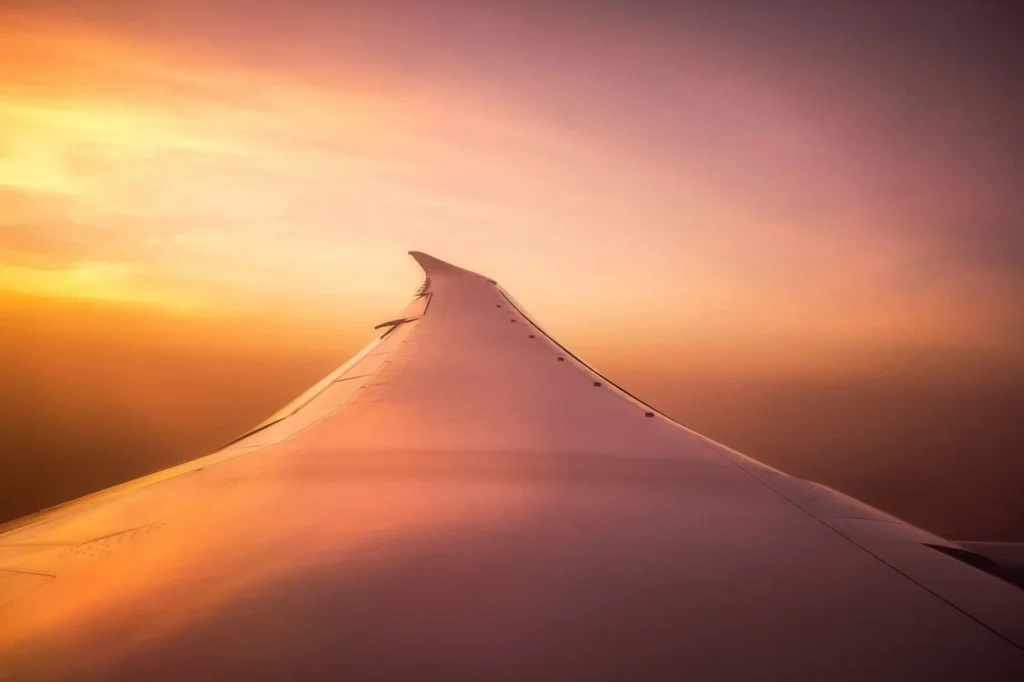 View of an airplane wing above the clouds at sunset